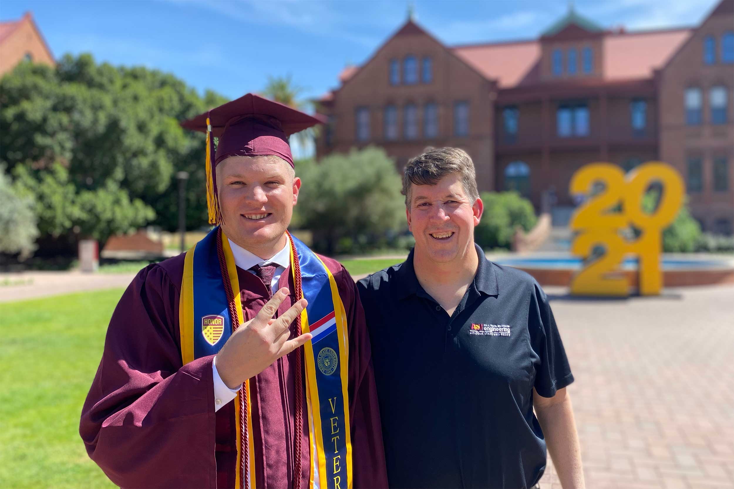 Fulton Schools Graduate Bobby Hudson, in his full regalia, including his veteran's stole, stands with his father, Rick, a Fulton Schools alumnus, in front of Old Main on ASU's Tempe campus