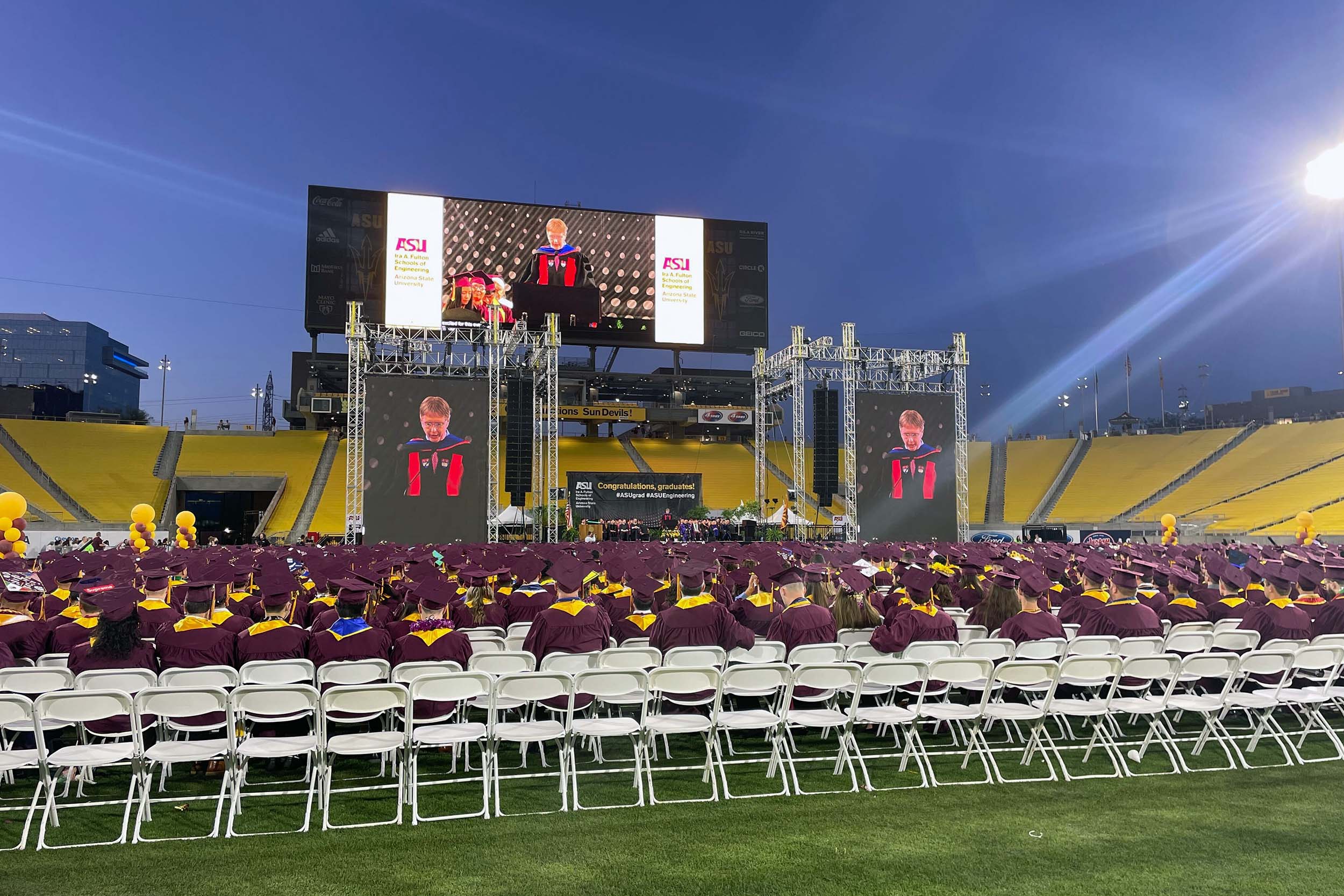 The 3,053 Spring 2022 ASU Engineering graduates stand on the field of Sun Devil Stadium at the end of Convocation in their caps and gowns, listening to Dean Kyle Squires at the podium